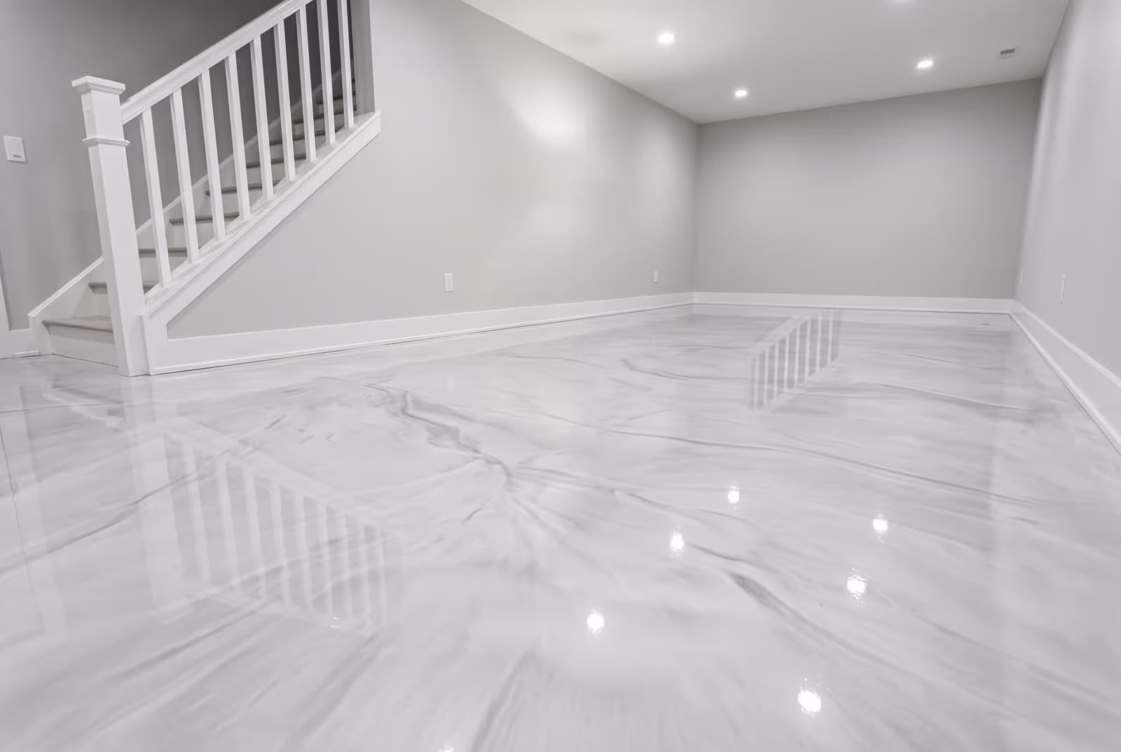 Pearl-white metallic epoxy floor at the base of a basement staircase