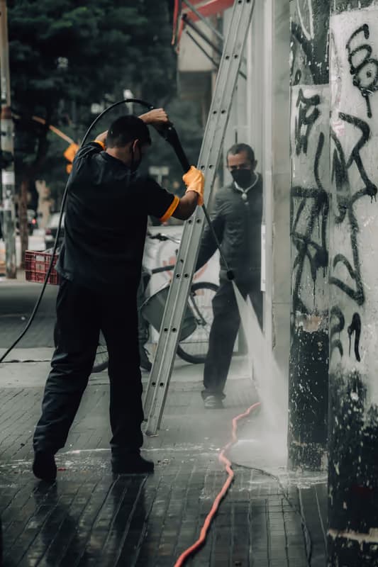 Crew pressure washing a storefront pillar and sidewalk — grime and paint lifting off