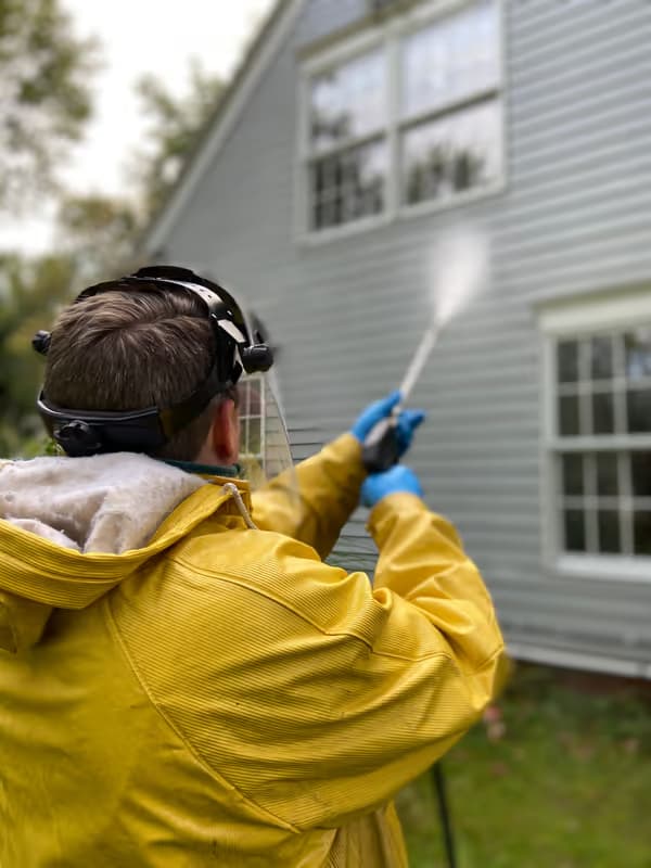 Technician spraying a home's siding clean — house exterior wash in progress